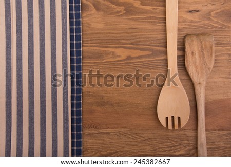 Wooden kitchen utensils and linen kitchen towels on dark wood tabletop, with copy space in the center