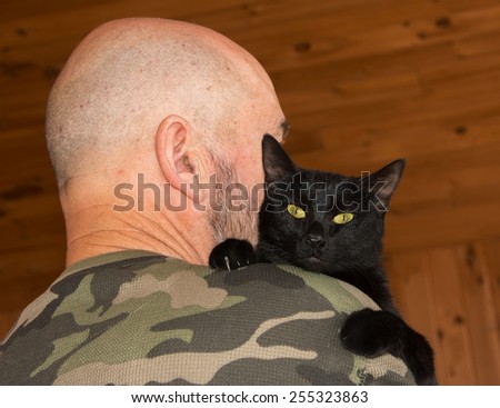 Middle-aged man with his black cat looking over his shoulder at the viewer