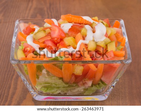Appetizer salad with lettuce, tomato, carrots and pickles topped with dressing, on dark wooden table