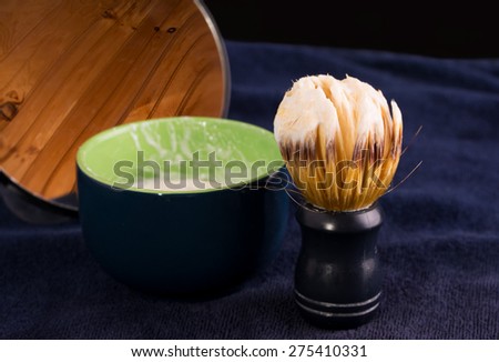 Shaving brush with foam, soap cup and mirror on dark blue towel