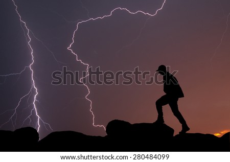 Silhouette of a man climbing on top of a mountain against a colorful sunrise