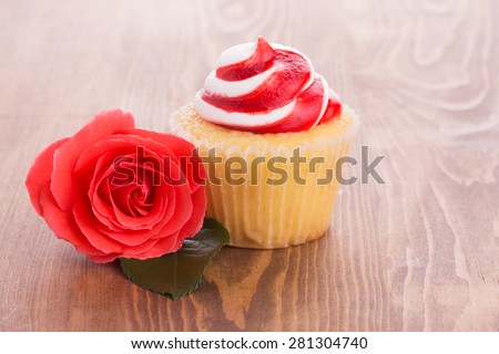 Strawberry cupcake with a beautiful red rose on wooden table, a simple treat to a loved one