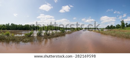 Panorama of a rural road completely inundated with flood waters, with pasture land on the left under water after heavy rains