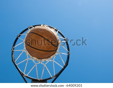 Basketball in net against blue skies - successful end to hard work - abstract concept of reaching one\'s goals, with copy space