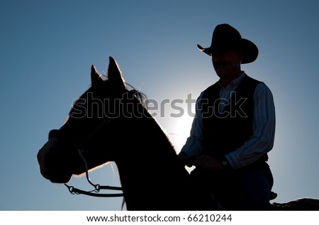 Rider in a cowboy hat and a horse silhouetted against sun and clear blue sky