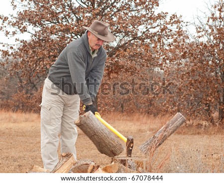 Middle-aged man chopping fire wood with an ax on a cold late fall day