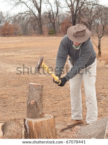 Man splitting wood with an ax on a gray, cold late fall day