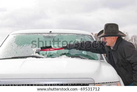 Middle-aged man scraping ice off his vehicle windshield on a cold winter morning after an ice storm
