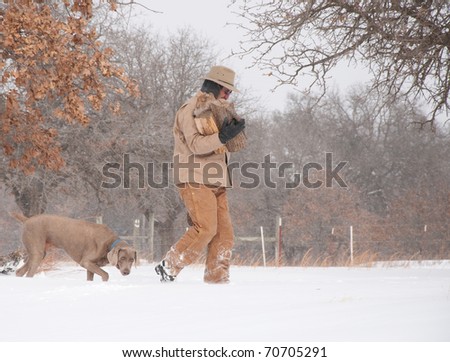Man carrying firewood bundled up in warm winter clothes, with his dog following in heavy snow fall