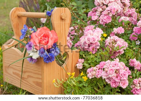 A wooden carrier box with spring flowers, against floral background with pink mini roses