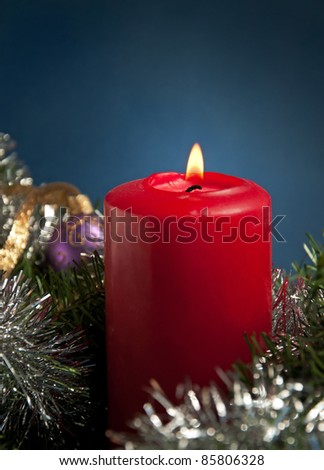 Red Christmas candle burning, surrounded by shiny silver tinsel, against blue background