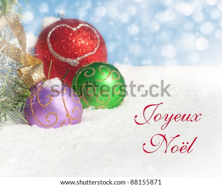 Dreamy image of colorful Christmas ornaments in snow with text Joyeux Noel, Merry Christmas in French