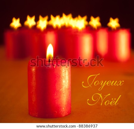 Red Christmas candle - with group of similar candles on background with stars for flames; with text Joyeux Noel, Merry Christmas in French