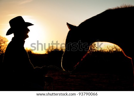 Silhouette of a man and his horse against sunset sky, with horse reaching towards man