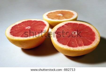 Three sliced red grapefruits on a white flat surface.