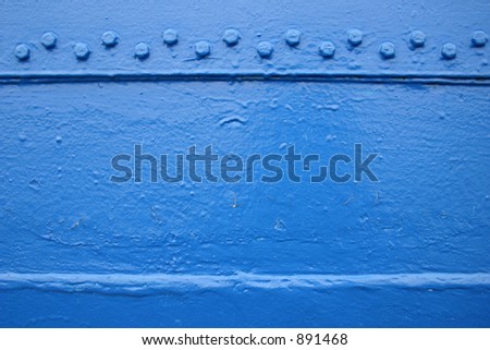 Blue painted ship\'s metal board with rivets on the upper edge.