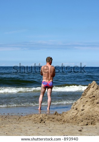 Man looking at the sea, wearing swimming trunks with american flag.