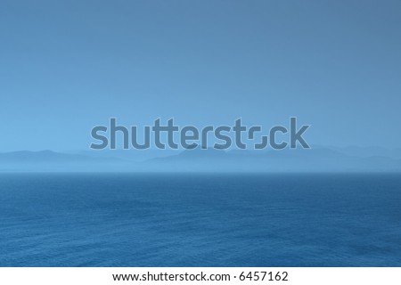 Blue seascape with foggy coastline mountains at the horizon. Toned background image.