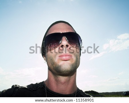male model with sunglasses and hat on standing out side looking towards camera