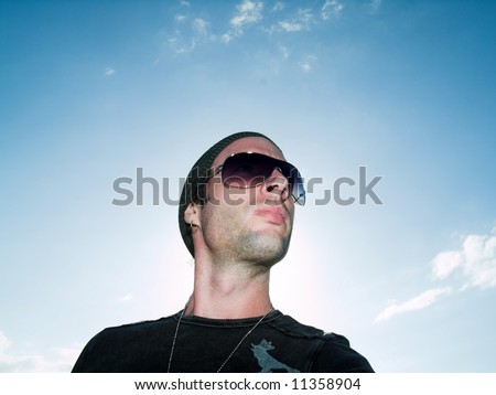 male model with sunglasses and hat on standing out side looking to the LEFT
