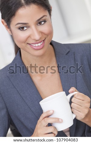 Beautiful young Latina Hispanic woman or business woman smiling, relaxing and drinking a cup of tea or coffee in her office