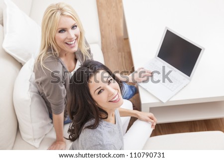 Overhead photograph of two beautiful young women at home sitting on sofa or settee using a laptop computer and smiling