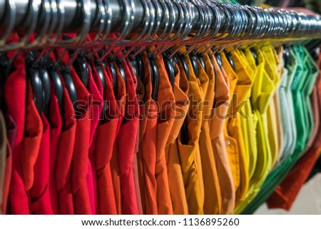 Male men’s shirts sorted in color order on hangers on a thrift shop or wardrobe closet rail
