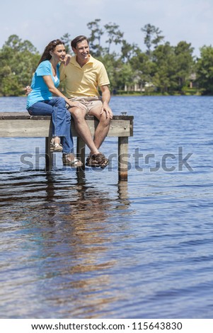 Portrait shot of an attractive, successful and happy middle aged man and woman couple in their thirties, sitting together on a jetty or pier by a lake