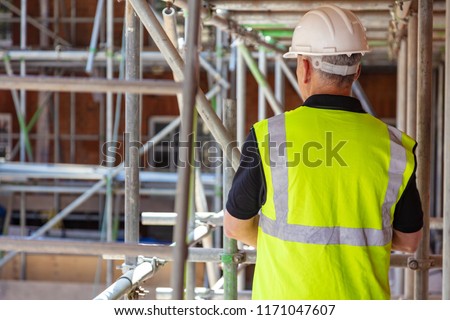 Rear view of male builder construction worker on building site wearing hard hat and hi-vis vest