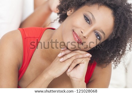 A beautiful mixed race African American girl or young woman laying down on a sofa wearing a red dress looking happy