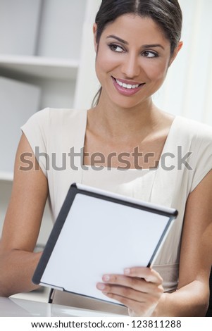 Beautiful young Latina Hispanic woman or businesswoman in an office and using a tablet computer