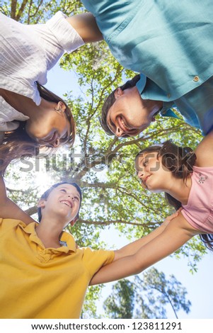 An attractive happy, smiling family of mother, father, son and daughter hugging in a huddle together outside in a park enjoying warm summer sunshine