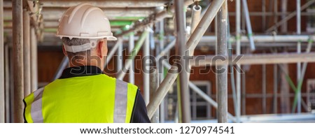 Rear view of male builder construction worker on building site wearing hard hat and hi vis vest panoramic web banner