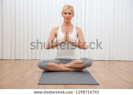 Beautiful woman young female hands in prayer practicing cross legged seated yoga pose indoors at a gym or health spa