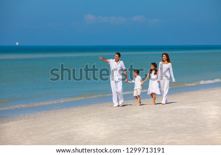 Happy family of mother, father and two children, son and daughter, walking holding hands and having fun in the sand on a sunny beach