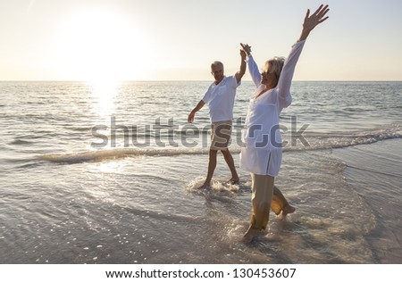 Happy senior man and woman couple dancing and holding hands on a deserted tropical beach at sunrise or sunset
