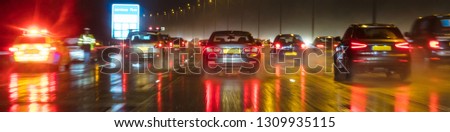 Panoramic web banner motion blurred photograph of traffic at in night in the rain on a British motorway with police officer and car