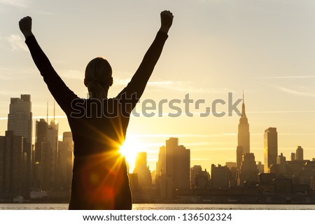 Silhouette of a successful woman or girl arms raised celebrating at sunrise or sunset in front of the New York City Skyline