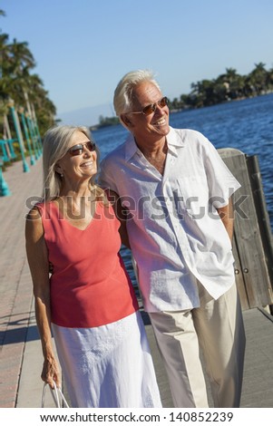 Happy senior man and woman romantic couple together looking out to tropical sea or river with bright clear blue sky