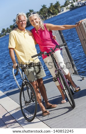 Happy senior man and woman couple together cycling on bicycles with bright clear blue sky by a river or sea