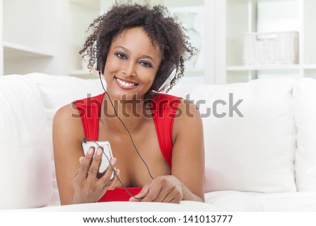 A beautiful mixed race African American girl or young woman laying down wearing a red dress listening to music on mp3 player and headphones