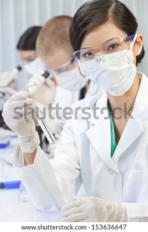 A Chinese Asian female woman medical or scientific researcher or doctor using looking at a test tube of clear liquid in a laboratory with her team