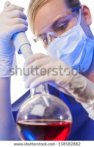 A female medical or scientific researcher or doctor using a pipette and flask of red liquid in a laboratory