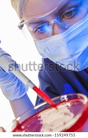 A female medical or scientific researcher or doctor using a pipette & petri dish blood sample in a laboratory