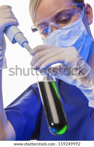 Female medical or scientific researcher or doctor using a pipette & test tube of green solution in a laboratory