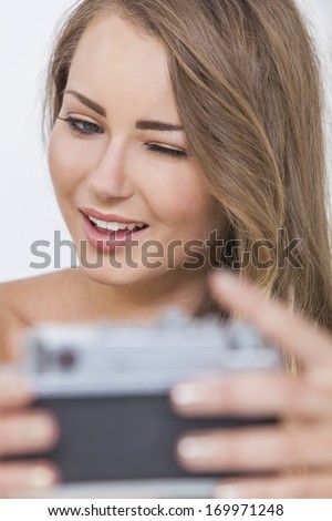 A beautiful naked blond girl or young woman winking and taking a selfie picture on a retro style digital camera