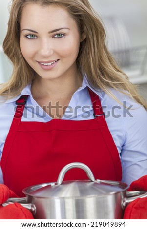 A blond girl or young woman looking happy wearing red apron & cooking in her kitchen at home