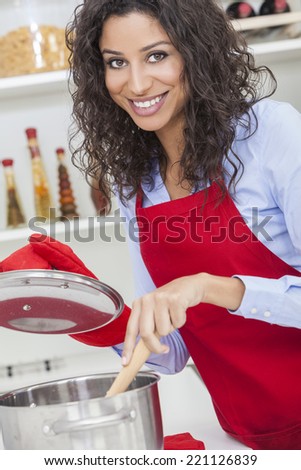 A beautiful girl or young woman looking happy wearing red apron & cooking in her kitchen at home