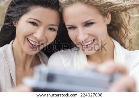 Two young women girls, one Asian Chinese, one blond, laughing taking selfie photograph with digital camera