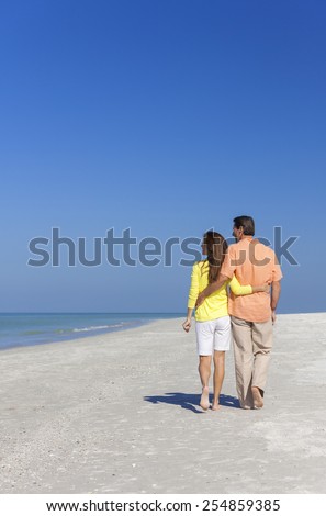 Rear view of man and woman romantic couple walking on a deserted tropical beach with bright clear blue sky